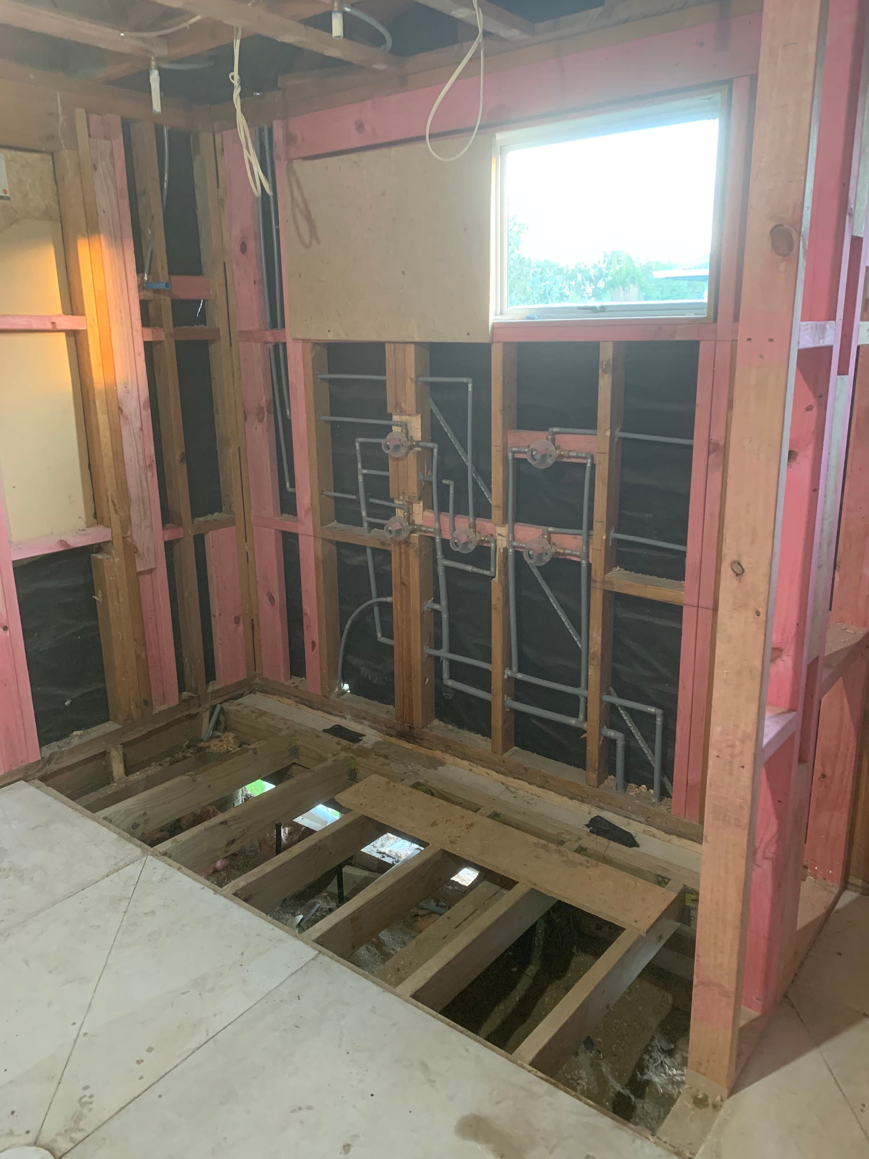 Bathroom rough-in showing hot/cold pipes and drainage in exposed framing